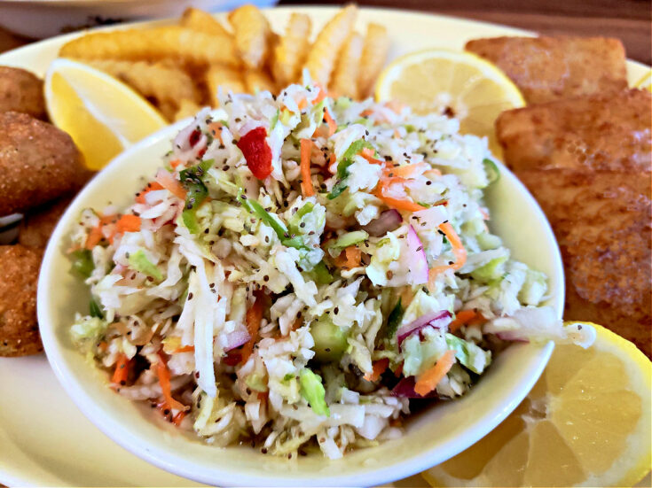 Old fashioned Amish overnight coleslaw recipe in a serving bowl with a seafood platter with fish, fries, and hushpuppies