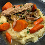 Easy Homestyle Crock Pot Pork Shoulder Roast Recipe served in a black bowl on a bed of creamy mashed potatoes