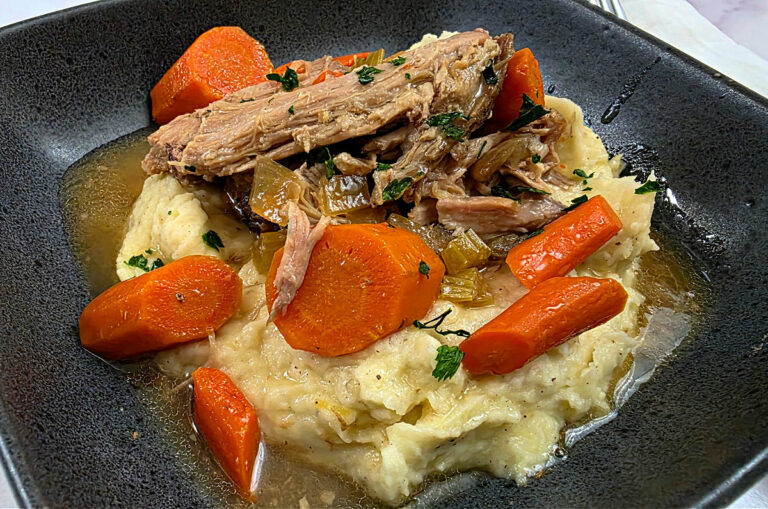 Easy Homestyle Crock Pot Pork Shoulder Roast Recipe served in a black bowl on a bed of creamy mashed potatoes