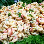 The Best Classic Macaroni Salad Recipe on a white serving platter garnished with fresh greens and scallions