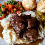 Mississippi Pot Roast served over mashed potatoes with peas, carrots and biscuits