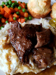 Mississippi Pot Roast served over mashed potatoes with peas, carrots and biscuits