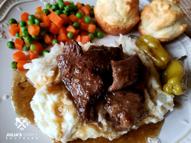 Mississippi Pot Roast served over mashed potatoes with peas, carrots and biscuits