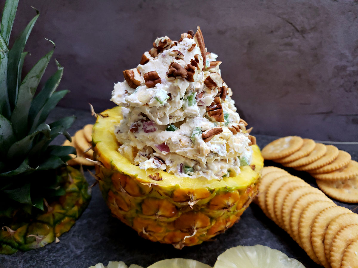 Easy Pineapple Cheese Ball Recipe with pecans, cheddar cheese, green pepper, onion, and seasoned salt served in a pineapple half with crackers