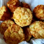 Easy Sour Cream Cheddar Cheese Biscuits Recipe in a bread basket wrapped in a white flour sack towel