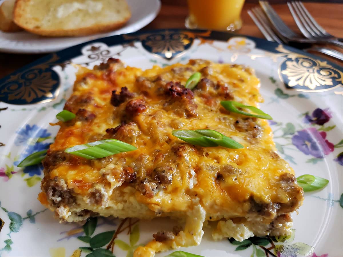 A serving of baked make ahead breakfast casserole on a Biltmore China plate with a slice of toast and orange juice