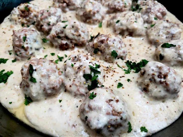 easy old fashioned meatballs and gravy recipe garnished with chopped parsley in a Lodge cast iron skillet