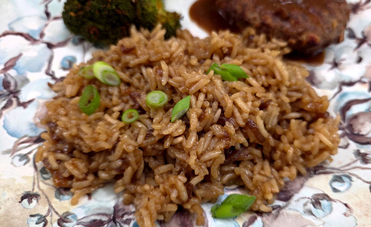 Beefy baked rice side dish on a plate served with hamburger steaks and steamed broccoli