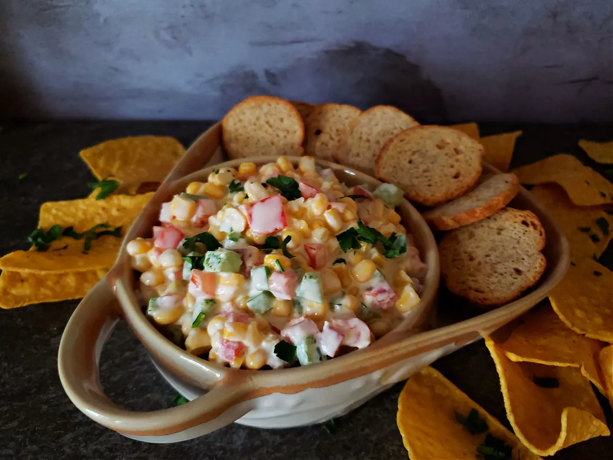 cold corn dip served in a serving bowl with tortilla chips and bagel chips