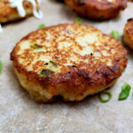 Easy old fashioned leftover mashed potato cakes recipe on a parchment lined serving tray garnished with sliced green onion and sour cream