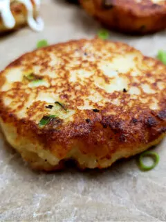 Easy old fashioned leftover mashed potato cakes recipe on a parchment lined serving tray garnished with sliced green onion and sour cream