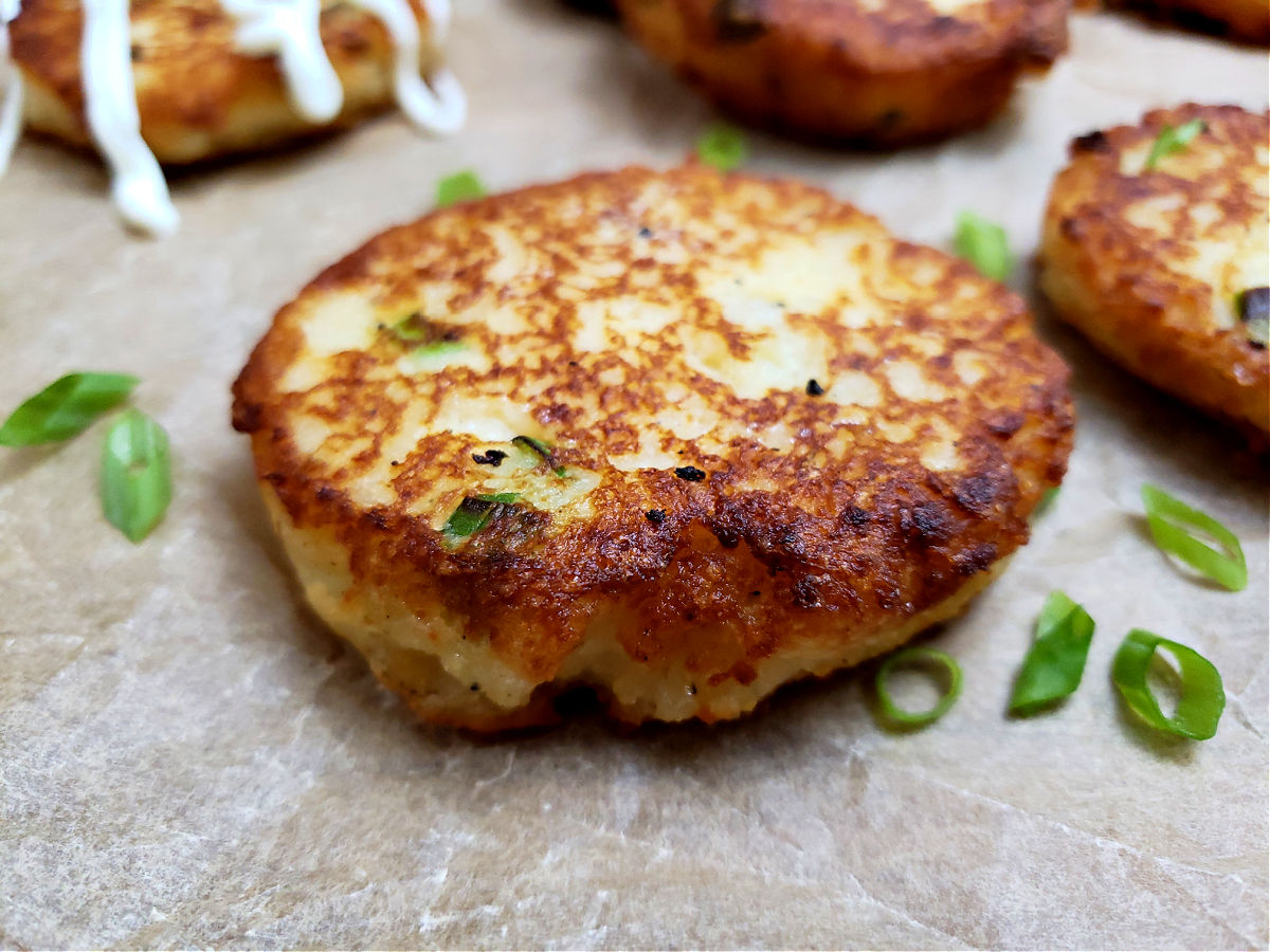 Easy old fashioned leftover mashed potato cakes recipe on a parchment lined serving tray garnished with sliced green onion and sour cream