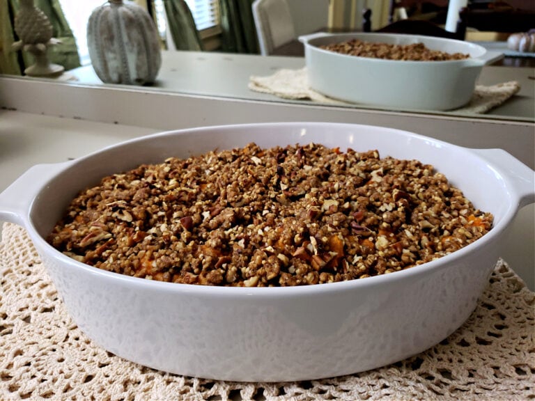 Sweet Potato Soufflé in w white oval casserole dish sitting on a buffet table with a mirror