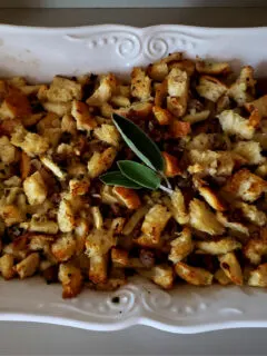 Old fashioned sausage stuffing, a Thanksgiving side dish, in a white baking dish with a wooden serving spoon. Garnished with fresh sage leaves