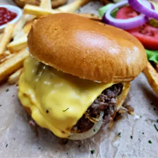 My favorite easy homemade smash burgers recipe served on a toasted bun with American cheese and caramelized onions with homemade fries