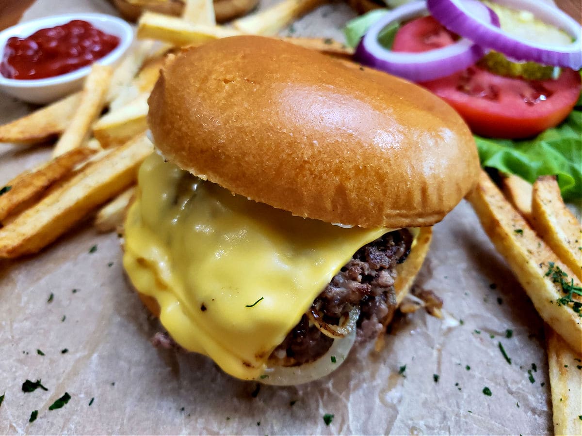 My favorite easy homemade smash burgers recipe served on a toasted bun with American cheese and caramelized onions with homemade fries