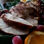 Juicy turkey breast tenderloin slices on a platter garnished with fresh herbs, citrus and fresh cranberries