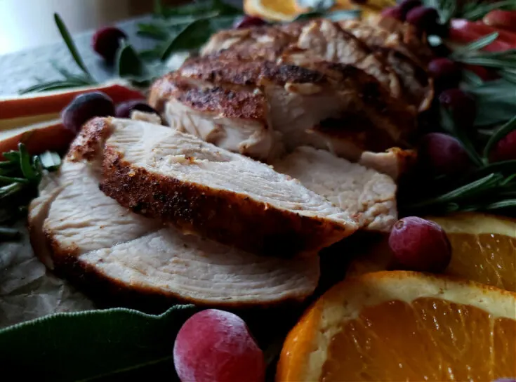 Juicy turkey breast tenderloin slices on a platter garnished with fresh herbs, citrus and fresh cranberries