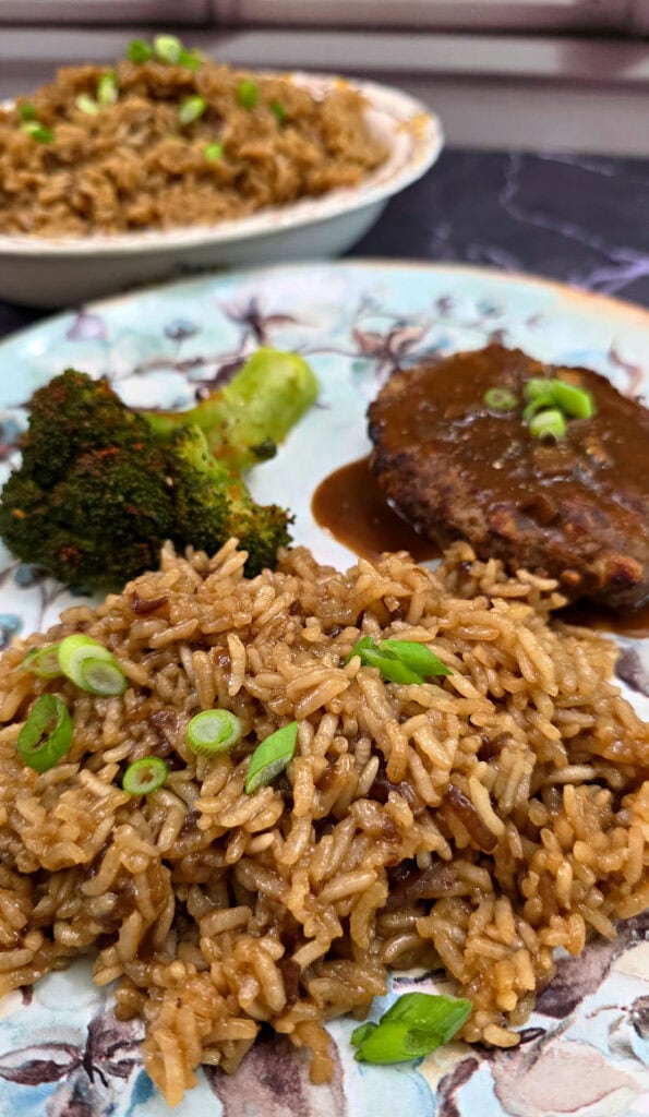 Blue dinner place with Southern baked brown rice serving with hamburger steak with gravy and steamed broccoli garnished with green onion slices