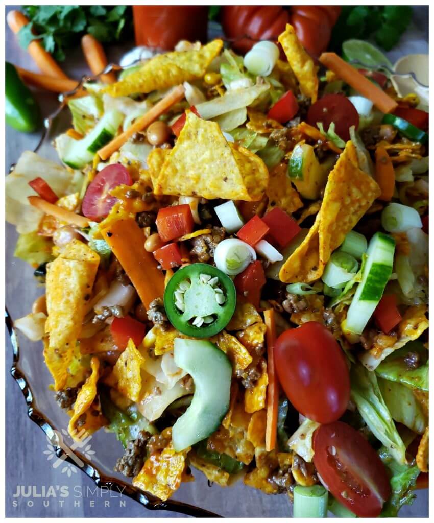 Layered Taco Salad tossed with Doritos in an amber glass bowl