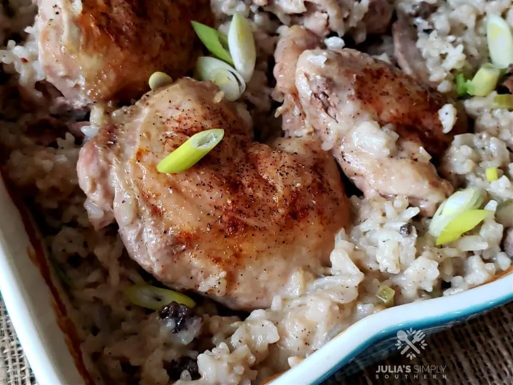Teal casserole dish with baked chicken and rice garnished with sliced spring onion