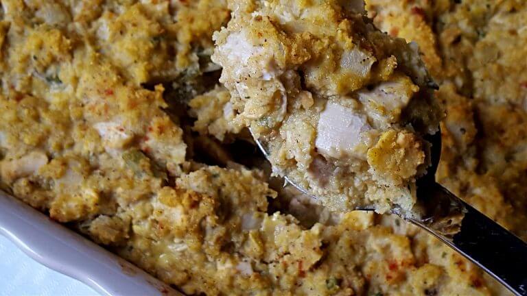 Serving spoon lifting out some chicken and cornbread dressing casserole from a baking dish