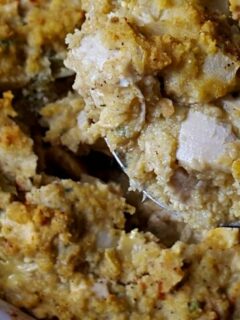 Serving spoon lifting out some chicken and cornbread dressing casserole from a baking dish