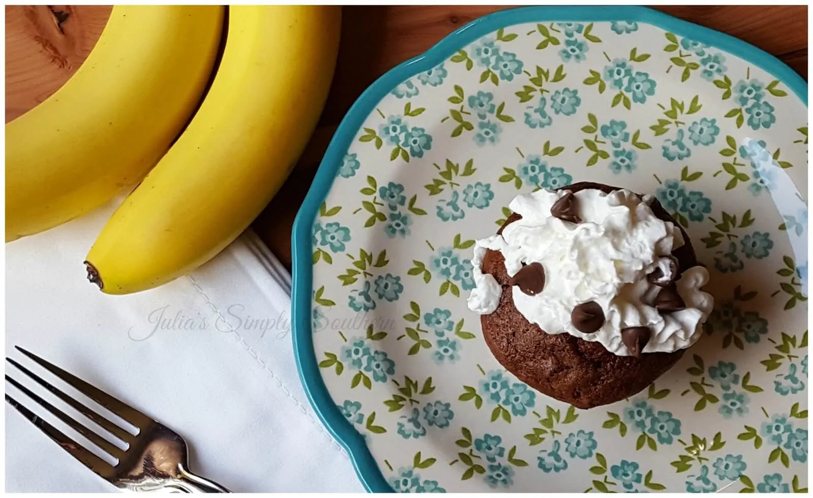 Homemade chocolate banana Muffins topped with whipped cream and chocolate chips on a floral plate.