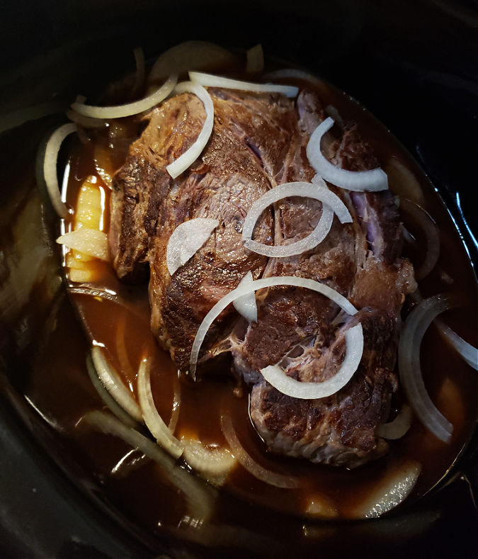 Crock Pot Barbecue chuck roast in liquid with sliced onions