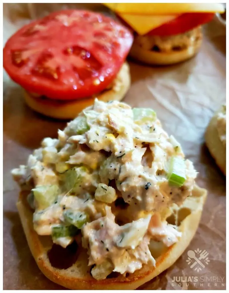Sheet pan with English muffins topped with tuna salad, tomato and cheese for a tuna melt before toasting in the oven