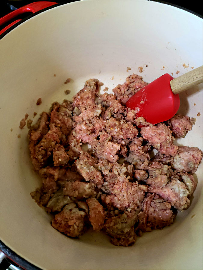 Minced breakfast sausage browning in a large red dutch oven