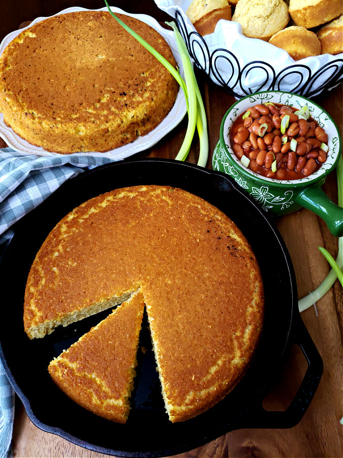 two cakes of cornbread and a basket of cornbread muffins with a bowl of pintos and green onions