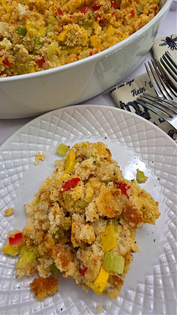 yellow squash dressing in a white oval baking dish with a serving on a white plate