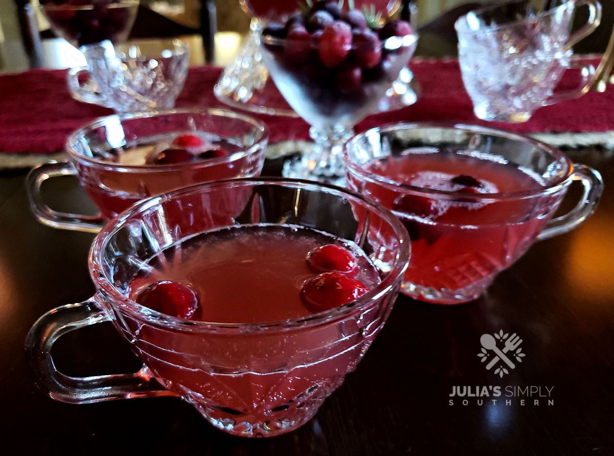 Cranberry Punch served in a crystal punch bowl garnished with frozen cranberries, fresh orange slices and served in crystal punch glasses