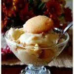 Glass dessert dish with homemade banana pudding in front of autumn flowers centerpiece on a dining table