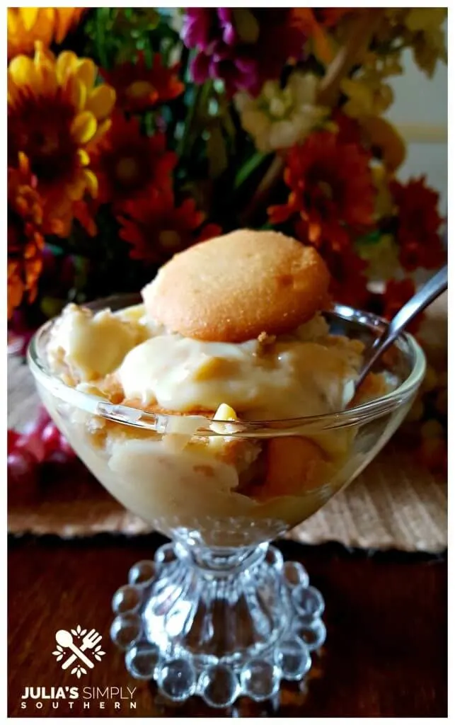 Glass dessert dish with homemade banana pudding in front of autumn flowers centerpiece on a dining table