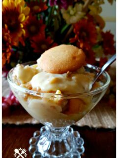 Glass dessert dish with homemade banana pudding in front of autumn flowers centerpiece on a dining table