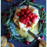 Slate platter with holiday Brie en Croute garnished with cranberry and rosemary served with crustini bread