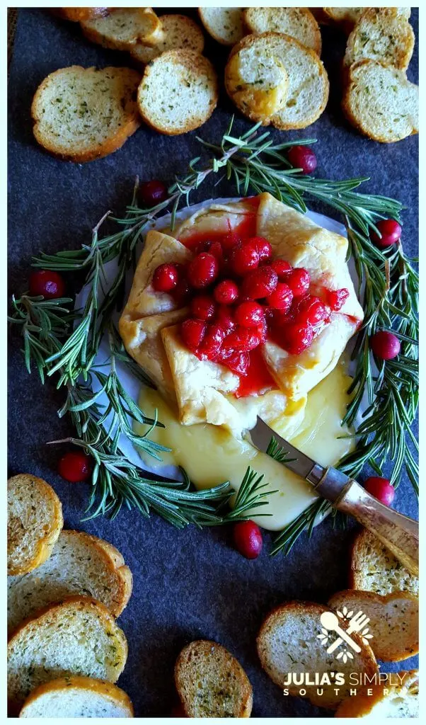 Slate platter with holiday Brie en Croute garnished with cranberry and rosemary served with crustini bread