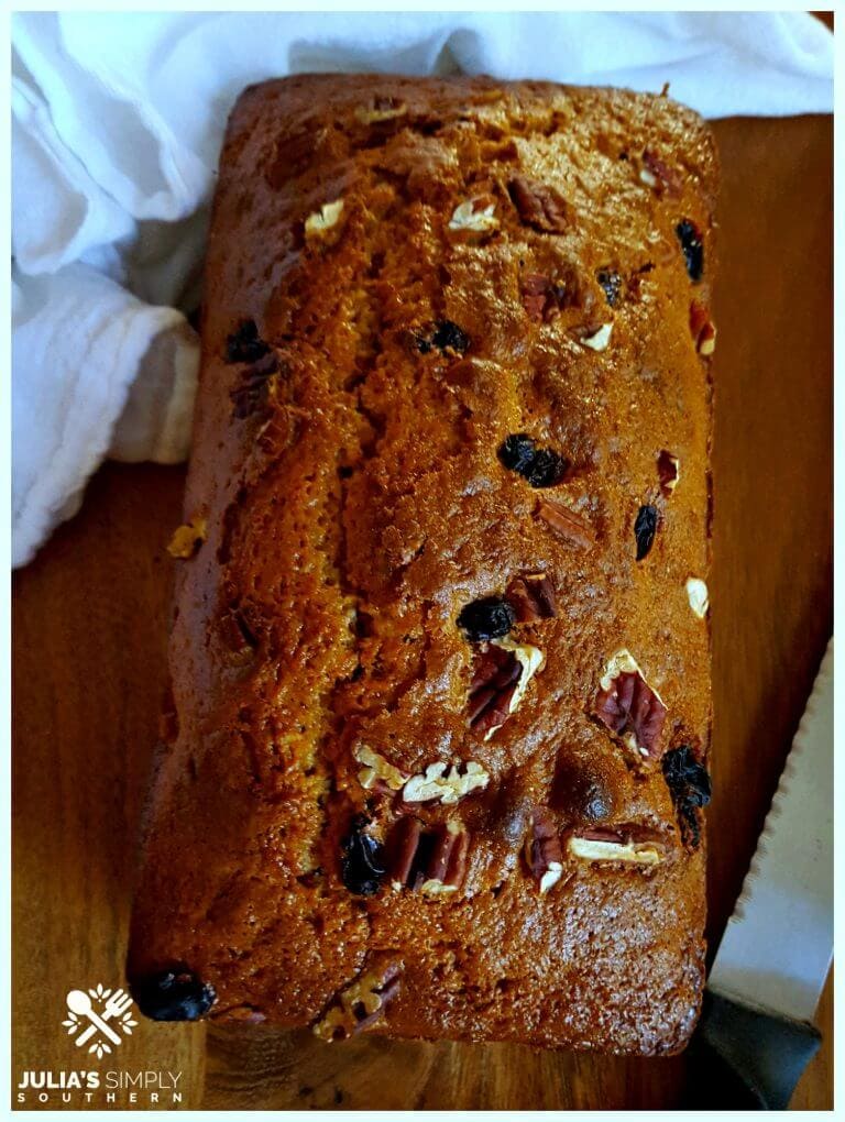 Southern Sweet Potato Bread on a wooden cutting board next to a bread knife and a white flour sack towel