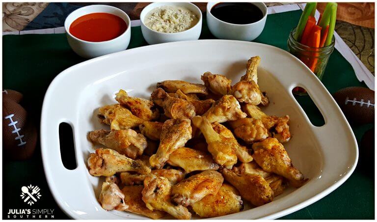 Baked Chicken Wings in a white platter for game day - Naked crispy baked wings served with buffalo, teriyaki and blue cheese dipping options along with celery and carrot sticks