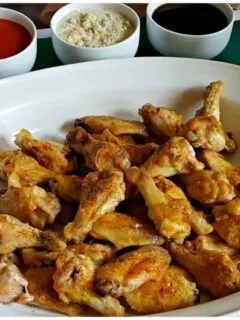 Baked Chicken Wings in a white platter for game day - Naked crispy baked wings served with buffalo, teriyaki and blue cheese dipping options along with celery and carrot sticks