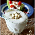 Clear glass serving dish filled with homemade blue cheese dressing and a wedge salad on a blue plate in the background