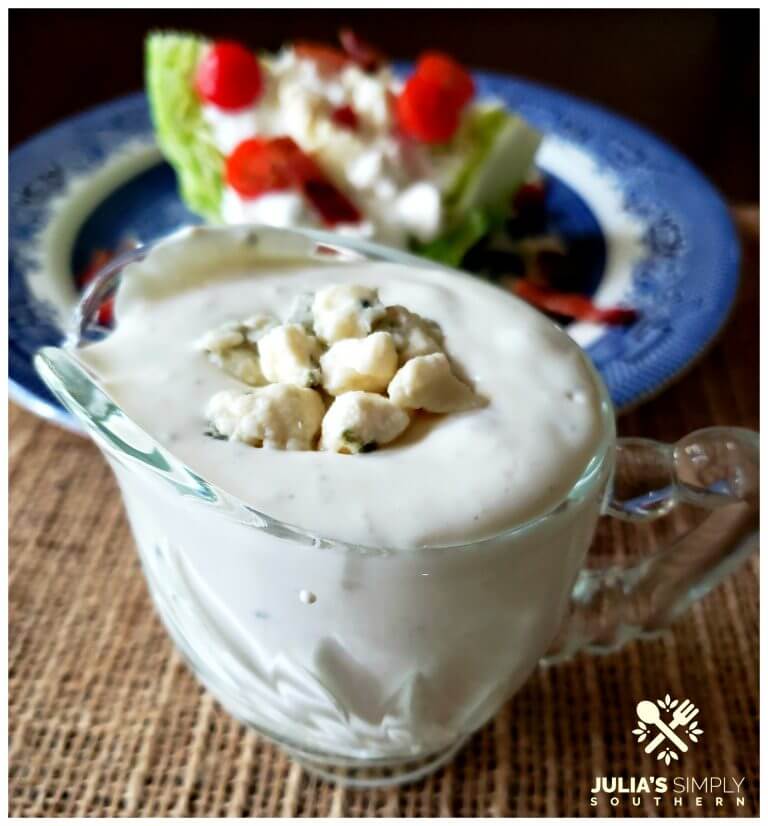 Clear glass serving dish filled with homemade blue cheese dressing and a wedge salad on a blue plate in the background