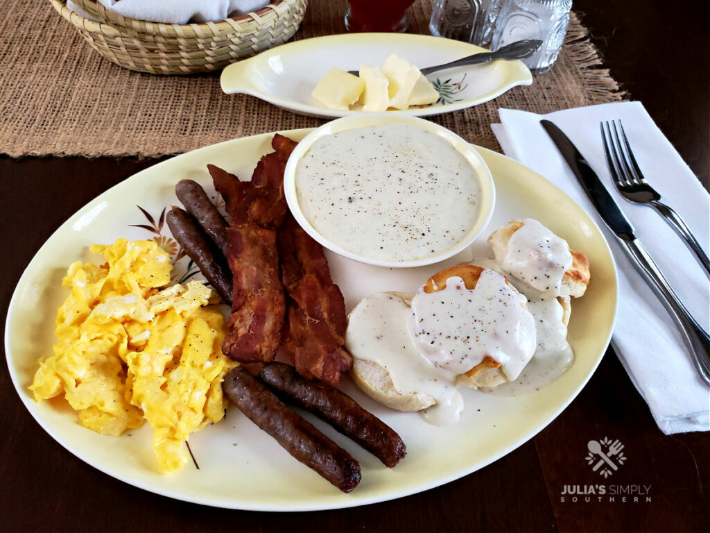 Homemade country white gravy on a breakfast plate with eggs, sausage and bacon with biscuits