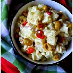 A serving bowl filled with potato salad with green olives and pimentos next to colorful napkins