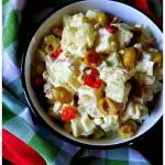 A serving bowl filled with potato salad with green olives and pimentos next to colorful napkins