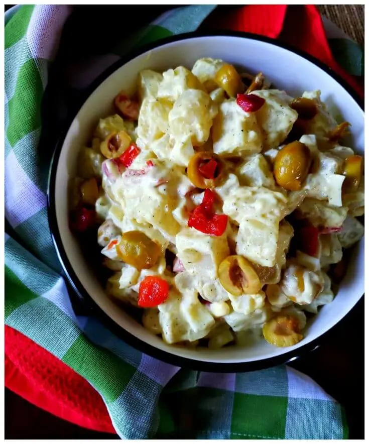 A serving bowl filled with potato salad with green olives and pimentos next to colorful napkins