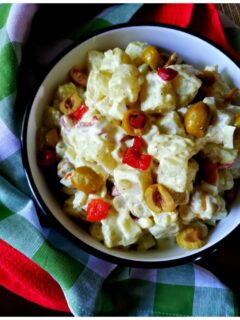 A serving bowl filled with potato salad with green olives and pimentos next to colorful napkins