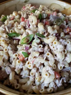 A large serving bowl with creamy tuna macaroni salad garnished with scallions